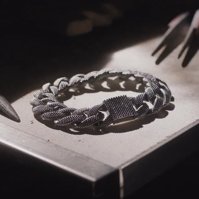 A chunky silver curb-chain bracelet with a dotted texture on a workbench.